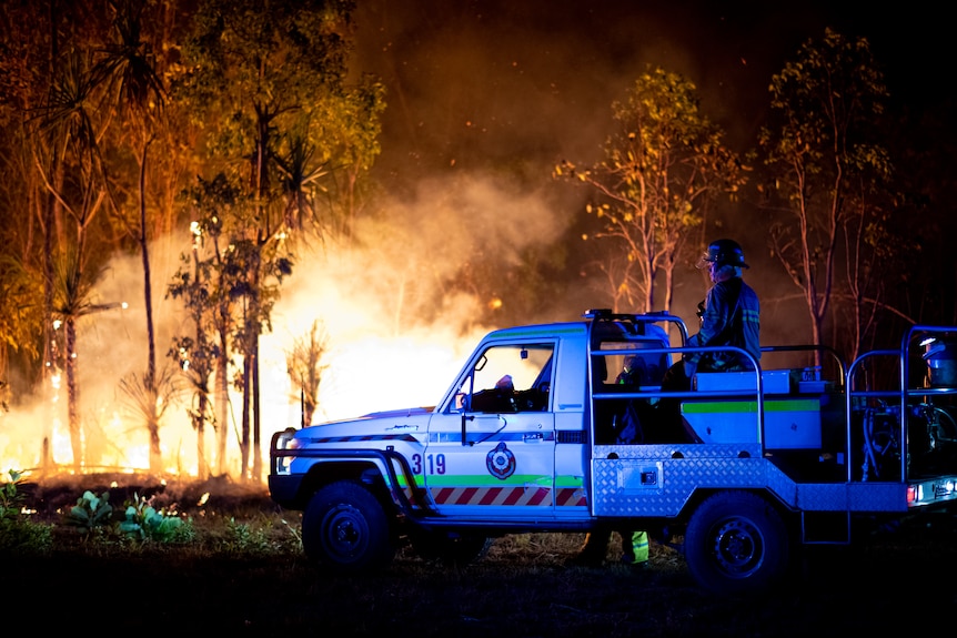 Police lights flash in front of a large bushfire at night.