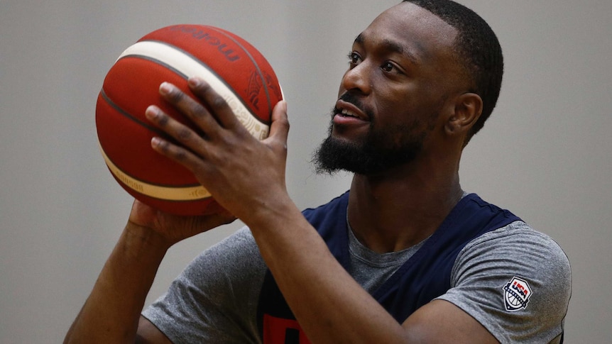 Kemba Walker holds a basketball in front of his face with a grey shirt on under a dark blue singlet