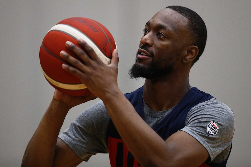 Kemba Walker holds a basketball in front of his face with a grey shirt on under a dark blue singlet