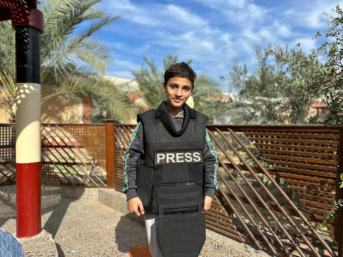 A boy wearing a bullet proof vest that says Press on it.