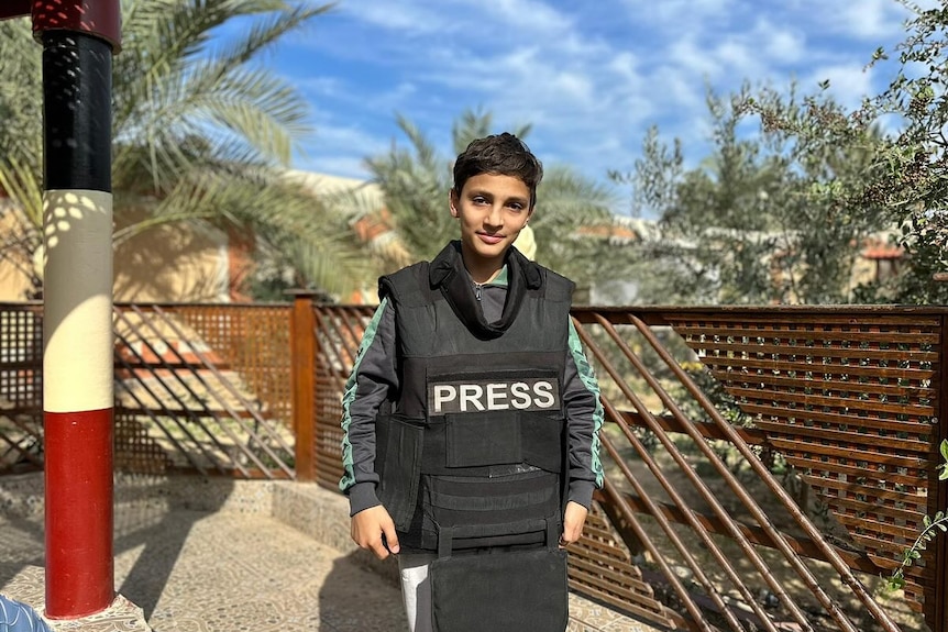 A boy wearing a bullet proof vest that says Press on it.