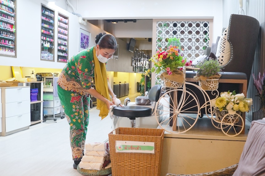 A Thai woman in a face mask wipes down a pedicure chair 