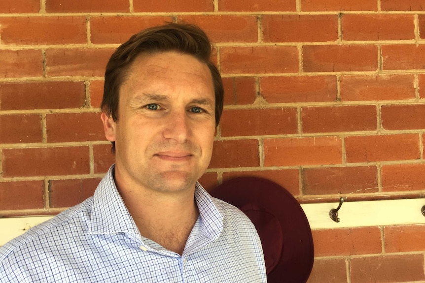 A man in a blue button up shirt standing in front of a brick wall.