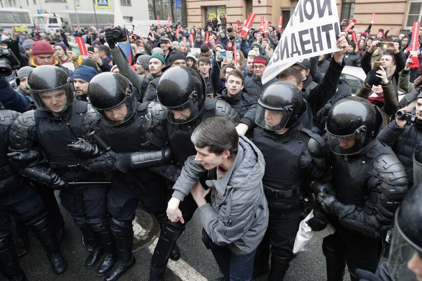 Riot police officers wearing helmets detain a protester during a rally in St Petersburg.