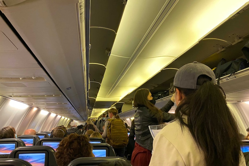 People packing their luggage on a plane, wearing masks