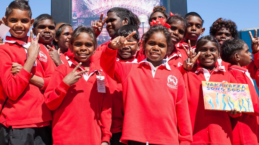 A group of students from Yakanarra Community School pose for a photo holding a illustrated book called Yakanarra Song Book.