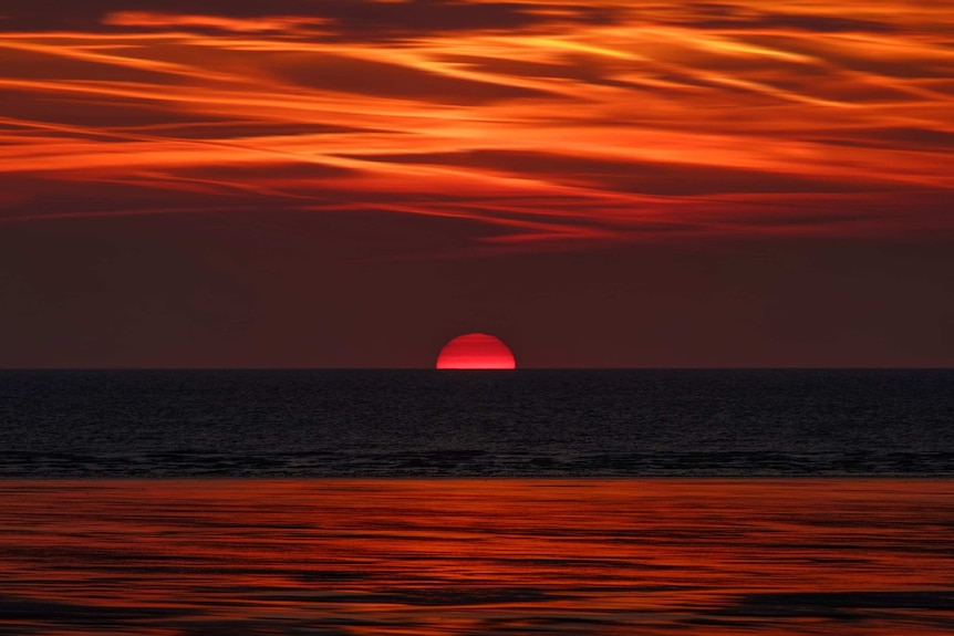 Red sun rising over water, with red skies.