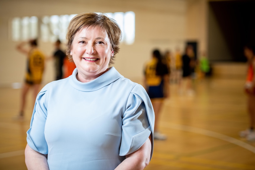 A woman smiling on a basketball court in a blue top.