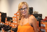 Woman smiles at camera with boxes of shoes lined up behind her