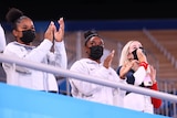 Three athletes cheer from spectator seats.