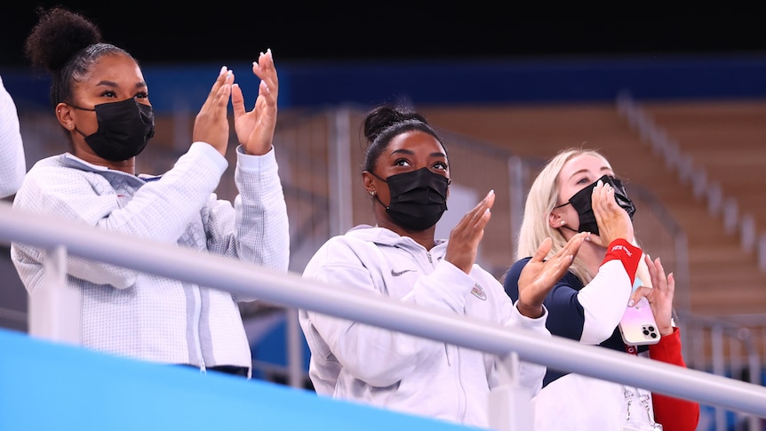 Three athletes cheer from spectator seats.