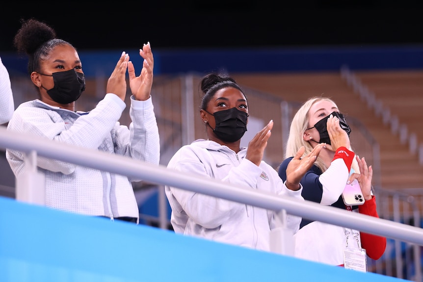 Three athletes cheer from spectator seats.