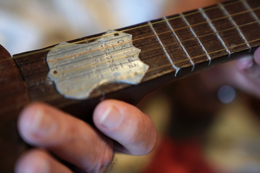 A close up of a metal plaque on the neck of a handmade ukelele.