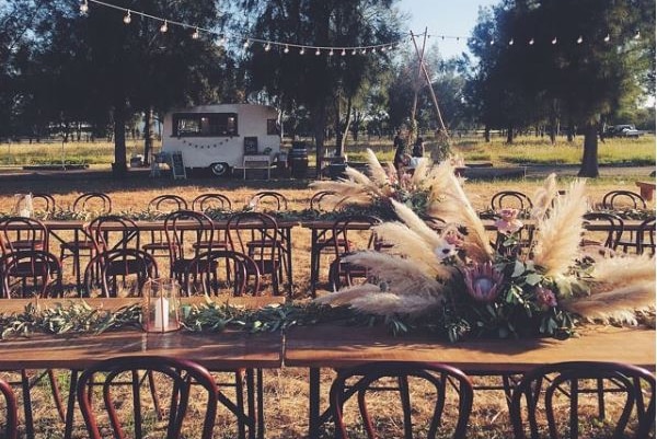 A floral arrangement containing weeds sits outside on a wedding table.