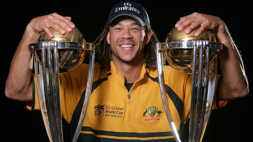 Andrew Symonds smiles while posing with two World Cup trophies