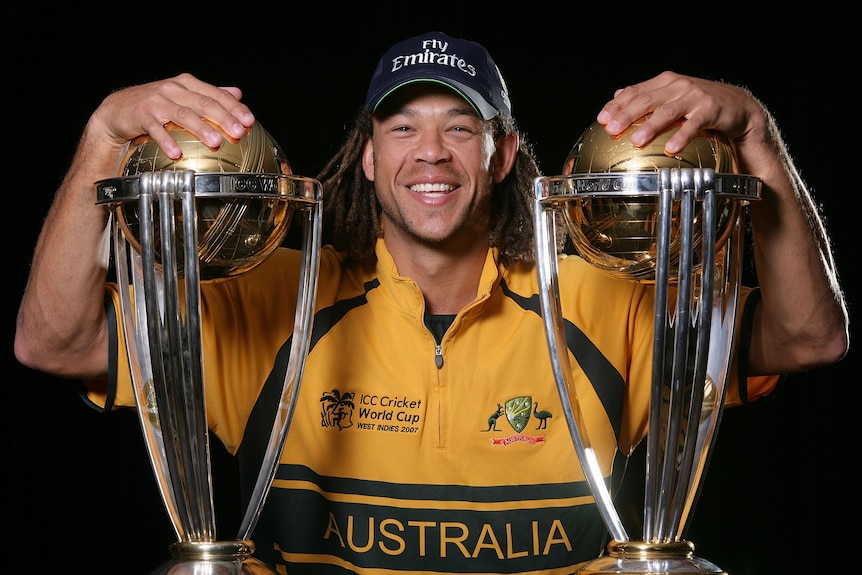 Andrew Symonds smiles while posing with two World Cup trophies
