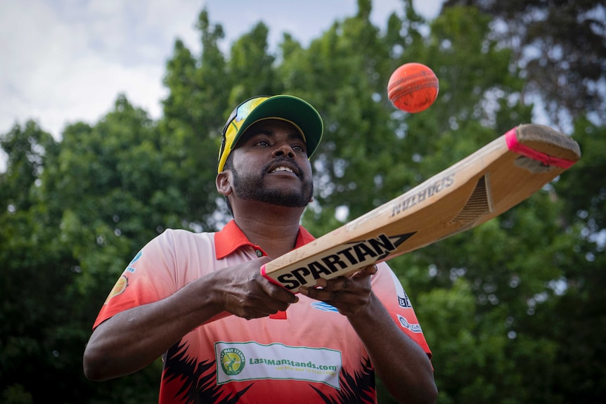 A Tamil cricket player kitting the ball of his bat, with stormy skies behind him.