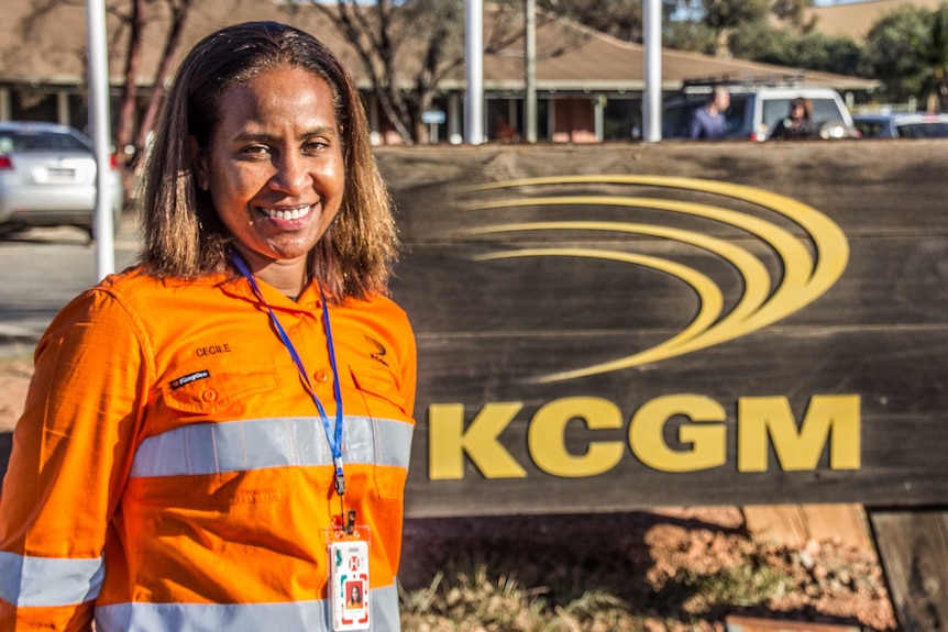 A woman in mining overalls smiles for the camera