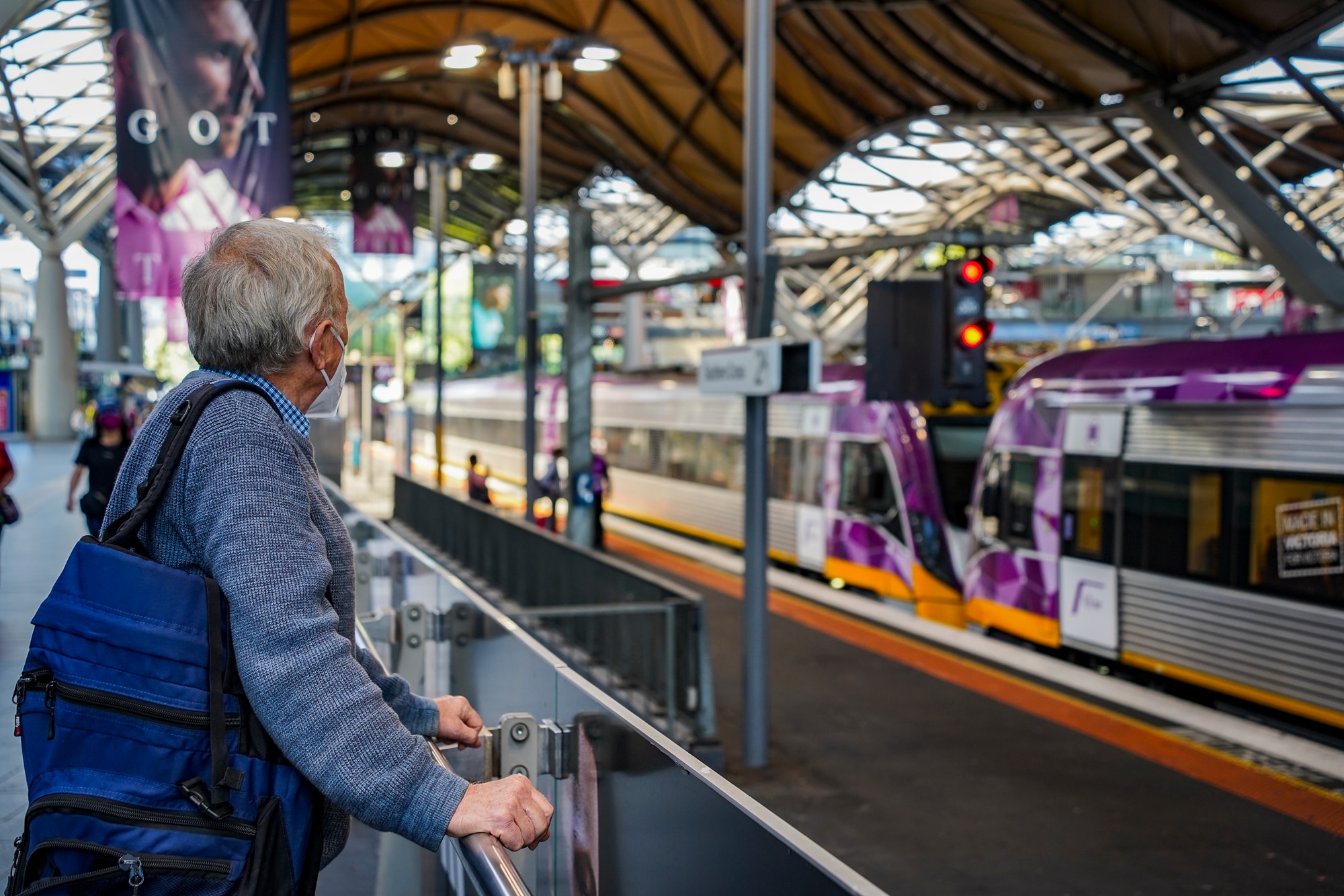 A man wearing a face mask is looking at a Southern Cross Station train platform