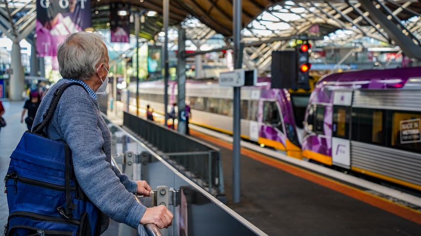 A man wearing a face mask is looking at a Southern Cross Station train platform