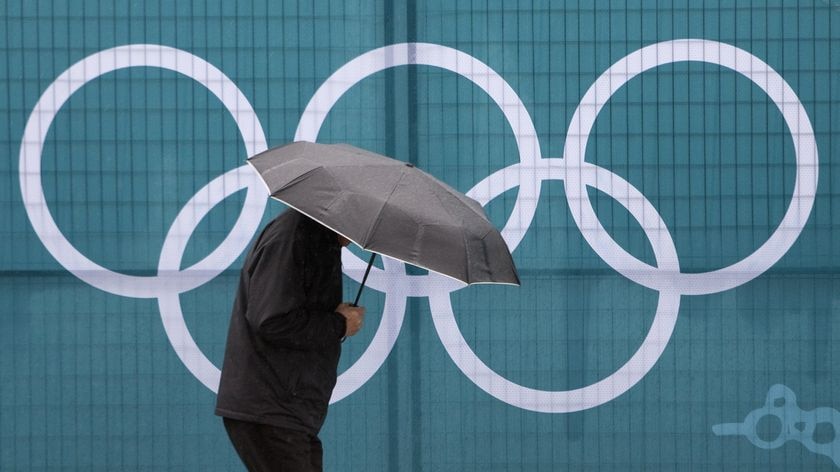 A pedestrian walks past an Olympic symbol while walking in the rain in Vancouver