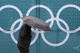 A pedestrian walks past an Olympic symbol while walking in the rain in Vancouver