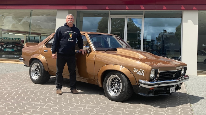 A man stands outside a Holden dealership with a bronze 1977 Torana.