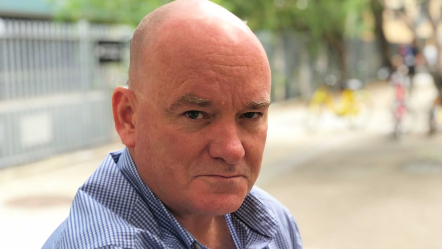 Brian Hartigan, in a blue shirt, looks down the barrel of the camera. He served with the Australian Army for 12 years.