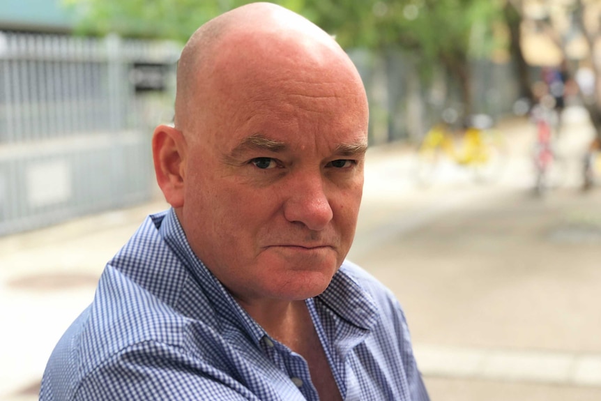 Brian Hartigan, in a blue shirt, looks down the barrel of the camera. He served with the Australian Army for 12 years.