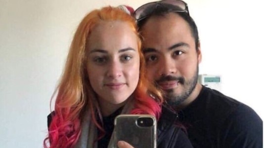 A woman with orange and pink hair next to a man with dark hair and beard taking a selfie