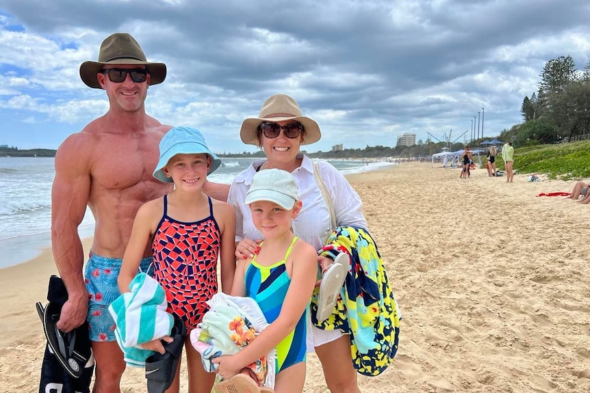 Man and woman smiling on beach, with two daughters in front of them