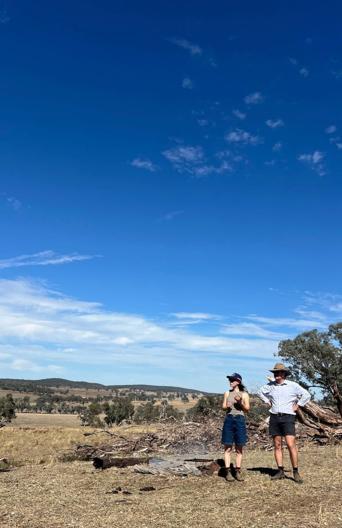 Two people standing on the land, looking to the left.