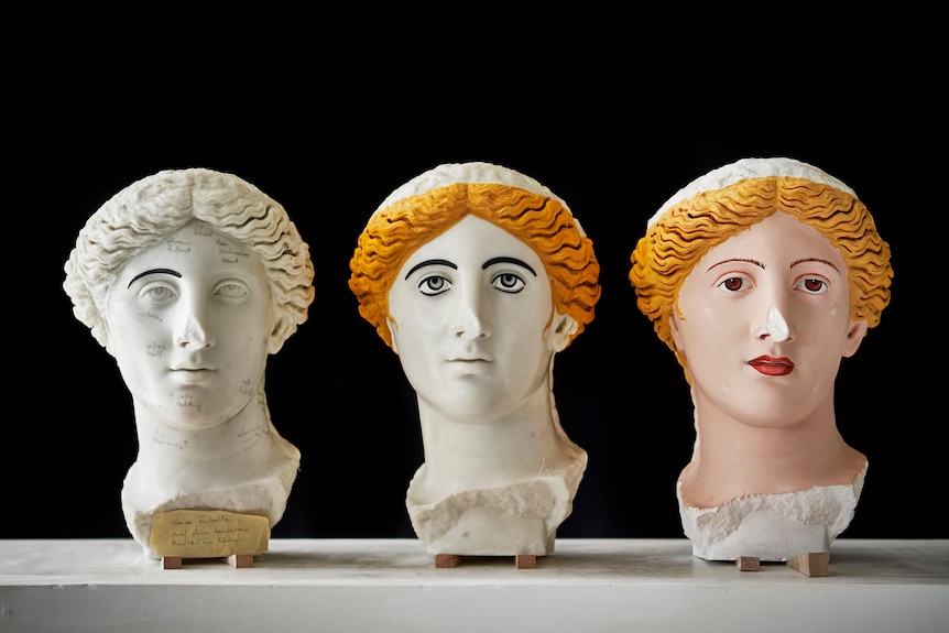 3 sculptured Roman heads, the 1st is white with one black eyebrow, the 2nd has black eyebrows + blonde hair & 3rd is in colour