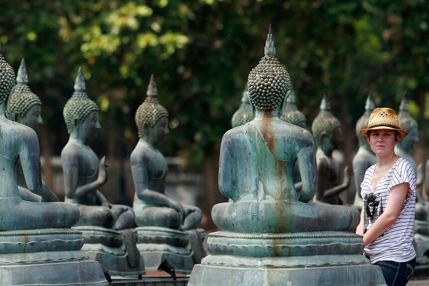 A woman wearing a straw hat looks at blue Buddha statues.