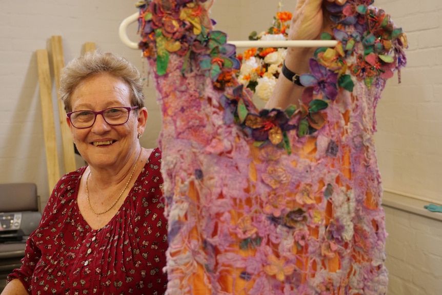 Julie Thornton holding up a colourful dress, smiling.