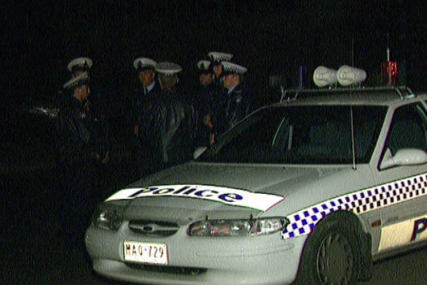 Seven police officers crowded around a white police vehicle