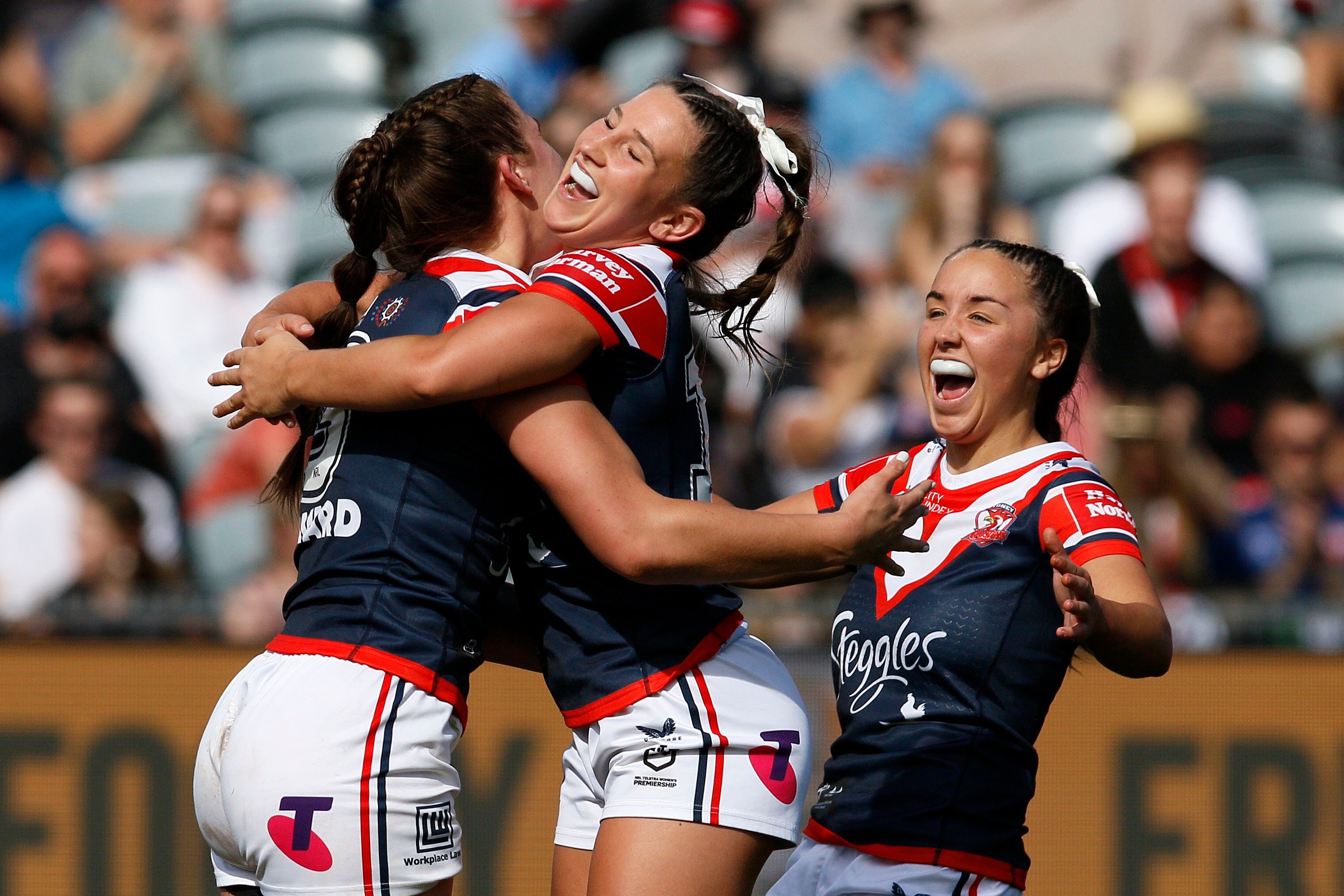 Three Sydney Roosters NRLW players embrace as they celebrate a try.