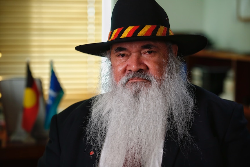 Dodson, with a long grey beard and wide brimmed hat marked with the colours of the Aboriginal flag.