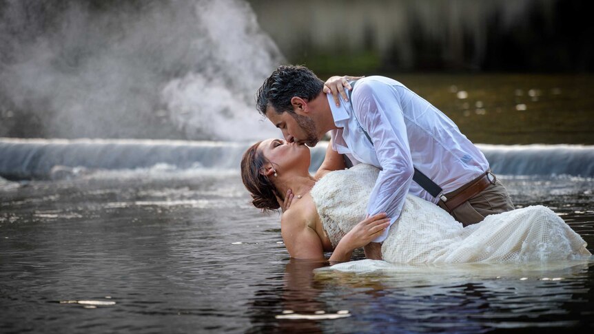 A man and a woman kiss during a photo shoot in a creek