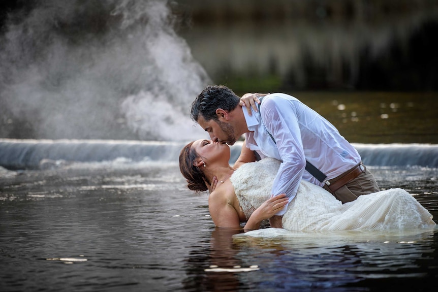 A man and a woman kiss during a photo shoot in a creek