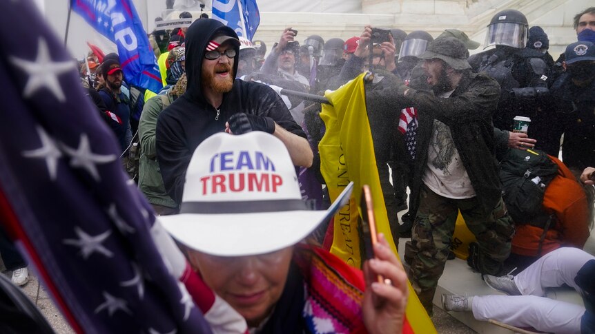Trump supporters, including a woman wearing a Team Trump hat, try to break through a police barrier.
