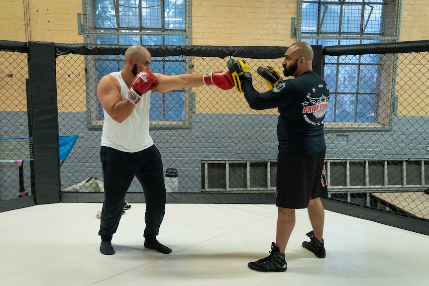 A man practices punching on a trainer inside a mixed martial-arts ring.