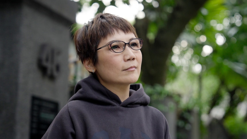 A middle-aged woman wearing a black hoodie and delicate glasses, with cropped hair