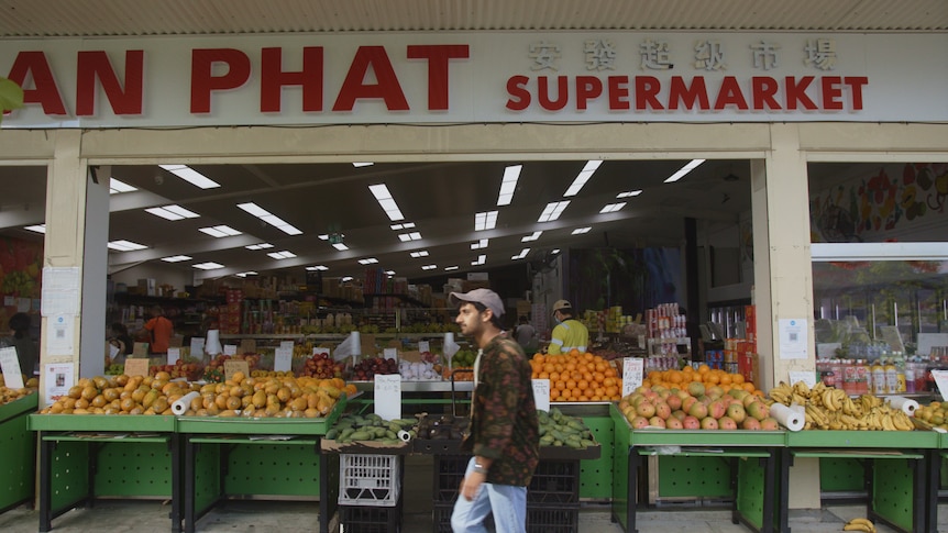 Arka Das walking past a market with oranges, bananas and fruits