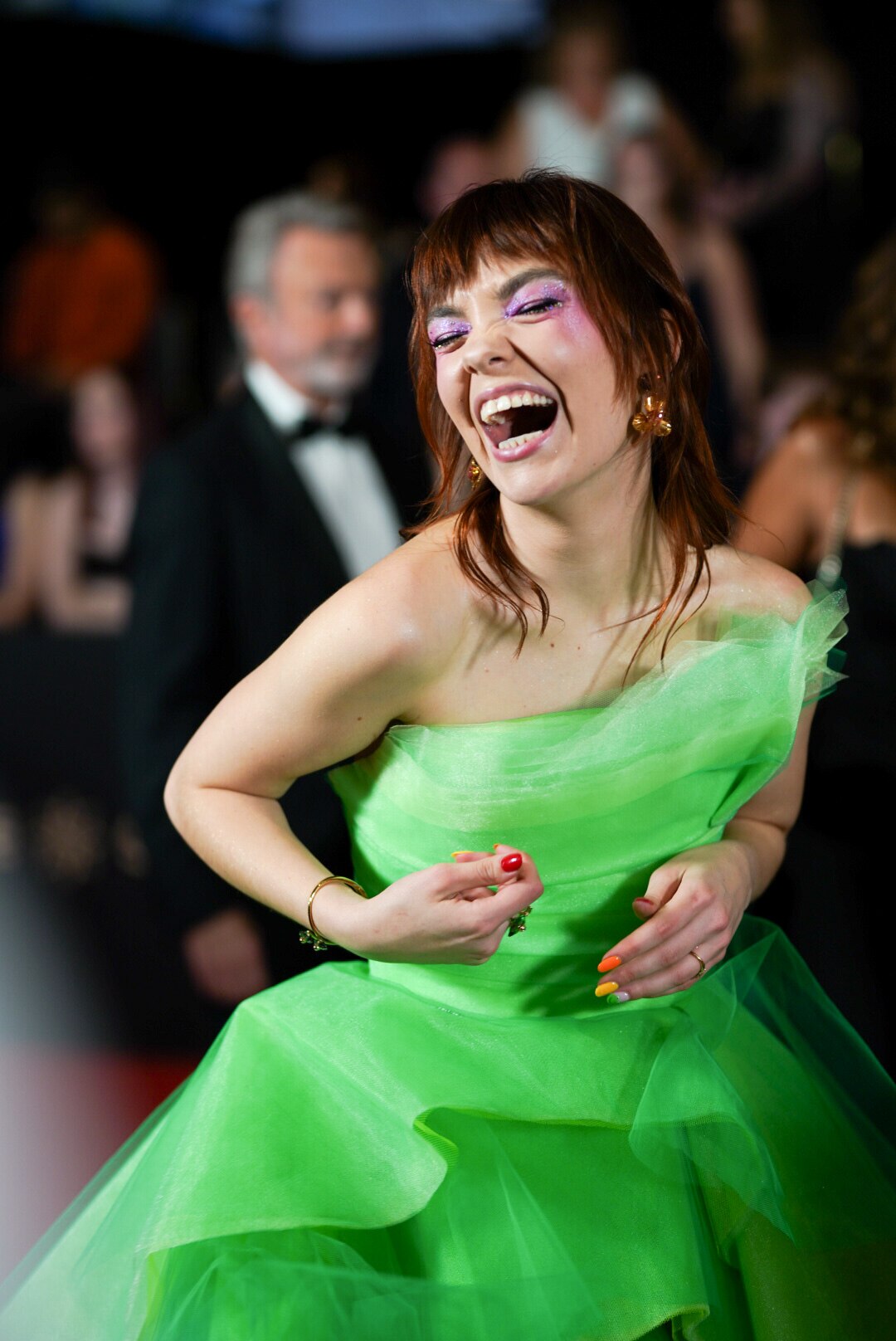 A woman in a neon green dress smiles on the red carpet