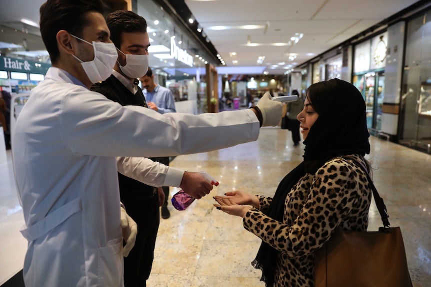 A woman has her temperature checked and her hands sprayed at a shopping mall