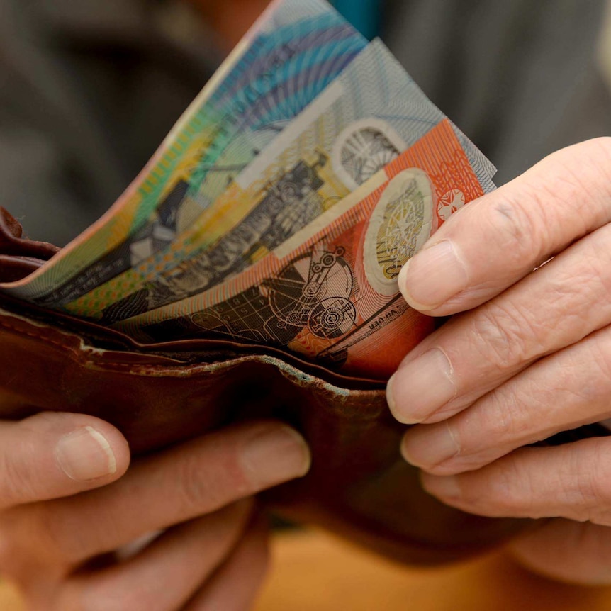 Hands put Australian currency into a wallet.
