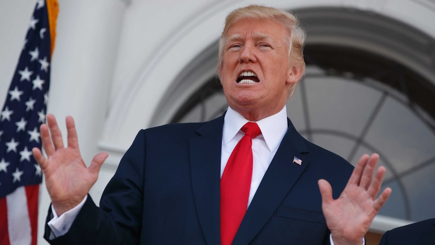 President Donald Trump speaks to reporters with his hands in the air.