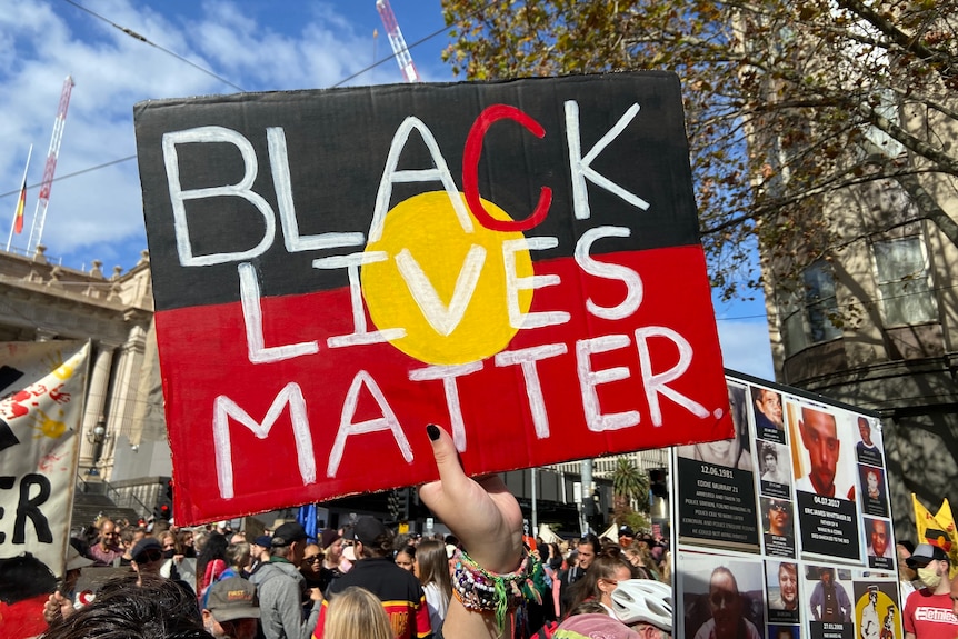 A protester holds a "Black Lives Matter" sign in front of a large crowd.