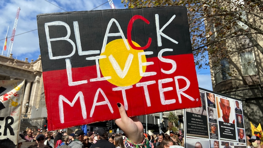 A protester holds a "Black Lives Matter" sign in front of a large crowd.